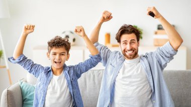 Yaşa! Duygusal baba ve oğul favori takımı destekliyor, TV 'de maç izlerken zafer için tezahürat yapıyorlar, golü el kaldırarak kutluyorlar. Aile birlikte boş zaman geçiriyor.