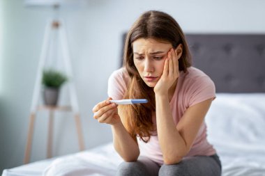 Üzgün genç bir kadın son hamilelik testini kontrol ediyor, evde yatakta oturuyor. Milenyum hanımefendisi istenmeyen çocuk doğurma ya da hamile kalamama gibi sorunlarla karşı karşıya.