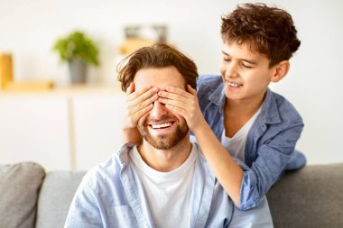 Bil bakalım kim oynuyor. Mutlu oğul babasının gözlerini elleriyle kapar, evde oynar ve eğlenir, birlikte vakit geçirir. Baba kanepede oturur, çocuk arkada durur.