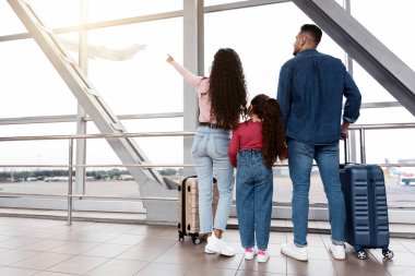 Havalimanında pencereden dışarı bakıp onları işaret eden üç kişilik bir aile, genç ebeveynlerin ve kızlarının terminalde bavullarıyla bekledikleri, uçuşu bekledikleri, fotokopi çektikleri,