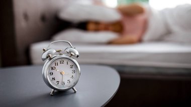 Yatağın yanındaki masada çalar saat ve uyanmak istemeyen genç bir kadının bulanık görüntüsü, yatakta yastıkla kulakları kaplayan, seçici odaklanma. Milenyum bayanı uykulu hissediyor, boşluğu kopyala