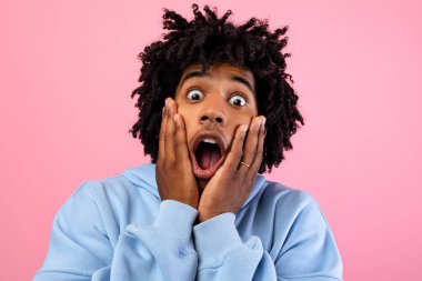 Havalı siyahi genç adam yüzüne dokunuyor, pembe stüdyo arka planında dehşet içinde bağırıyor. Afro-Amerikan ergen duyguları şok edici ya da korkmuş, korkunun duygularını ifade ediyor.