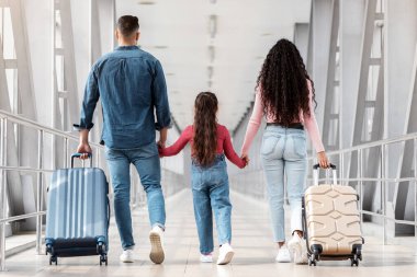 Havalimanında birlikte yürürken aile fotoğrafı, tanınmayan ebeveynler ve küçük kız el ele tutuşurken bavulları uçuş kapısına giderken görüntülendi.