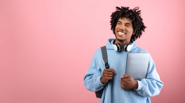 Sırt çantası, tablet bilgisayarı ve kulaklıkları olan, pembe stüdyo arka planında okuyan Afro-Amerikalı pozitif bir genç öğrenci. Uzaktan eğitim alan mutlu siyah ergenler.