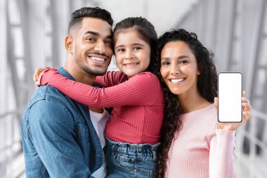 Cep telefonu reklamı. Havalimanı Terminali 'nde yan yana dururken üç kişilik neşeli Ortadoğulu Aile Yeni Uygulama, Moda Uygulaması,