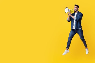 Havalı kotlu duygusal Arap bir adam hoparlörle zıplıyor, sarı stüdyo arka planından fotokopi odasına doğru bağırıyor, panorama. Mutlu Orta Doğulu stil adamı reklam yapıyor.