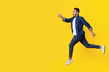 Heyecanlı orta doğulu genç adam sarı stüdyo arka planında fotokopi alanına doğru koşuyor, panorama. Mutlu yakışıklı Arap adam inanılmaz bir teklif alıyor, uzun bir fotoğraf.