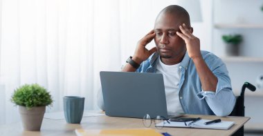 İşte sorunlar, zorluklar ve hatalar, aşırı çalışma. Kötü bir his ya da hata. Üzgün, orta yaşlı, tekerlekli sandalyede sakat bir adam dizüstü bilgisayara bakar, oturma odasının içindeki şakaklara dokunur.