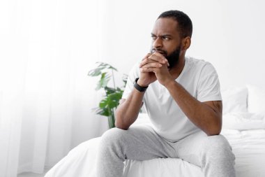 Mutsuz, genç, dalgın, siyah sakallı erkek yatak odasında iç tarafta, beyaz duvar arkasında, kopyalama alanında oturuyor. İnsan evdeki sorunları düşünür, kendini izole eden virüsler sırasında stres yapar.