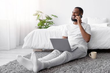 Afro-Amerikan sakallı genç adamın dizüstü bilgisayarda oturup yatak odasındaki müşteriyle telefonda konuşmasına sevindim. Başarı işi, sosyal mesafe, evdeki yönetici işyeri