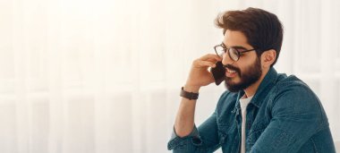 Mobil iş iletişimi ve girişimcilik. Arap işadamı cep telefonuyla konuşuyor ve dizüstü bilgisayar kullanıyor. Ev ofisindeki iş yerinde oturuyor. Boş bir alan.