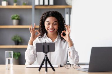 Covid-19 salgını, evde eğitim, mükemmel öğrenme sonuçları, sosyal mesafe ve çevrimiçi okula dönüş. Gülümseyen genç siyahi bayan öğretmen elleriyle işaret et, içerideki webcam 'e bak.