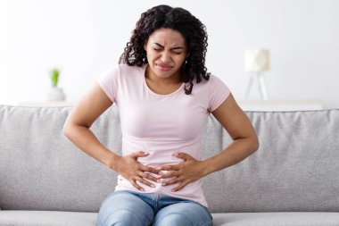 Hastalık, kötü his, mide sorunları, regl, hastalık ve zehirlenme. İç kısımlarında, gri iç kısımlarında, iç kısımlarında karın ağrısından muzdarip binlerce yıllık üzgün Afrikalı Amerikalı kadın.