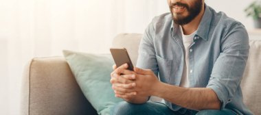 Mobil iletişim. Mutlu Arap adam evdeki akıllı telefondan mesajlar okuyor rahat oturma odasındaki kanepede dinlenirken, pozitif adam cep telefonu ekranına bakıyor, boş yer var.