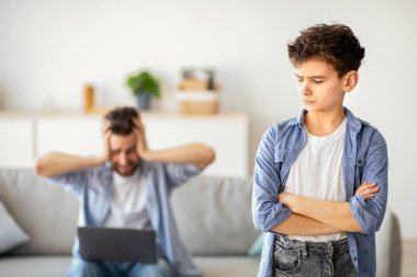 Ev sorununda çalış. Çocuk babama darılmıştı. Kızgın babası dizüstü bilgisayarda çalışırken, arka planda kanepede otururken elleri çapraz duruyordu. Nesiller yanlış anlama.
