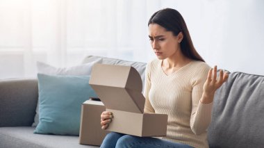 Covid-19 karantina, negatif insani duygular, bozuk mallar, hata, paketleri açmanın hayal kırıklığı. Huysuz, mutsuz, bin yıllık Arap kadın oturma odasındaki kanepede karton kutuya bakıyor.