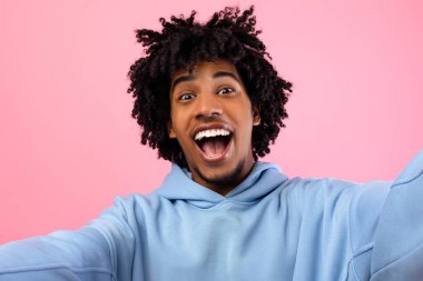 Heyecanlı genç zenci çocuk pembe stüdyo arka planında selfie çekiyor. Afro-Amerikan gençlerin kendi portresi. Mobil fotoğraf çekiyor, kameraya gülümsüyor, eğleniyor.