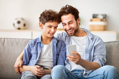 Aile aletleri konsepti. Mutlu baba oğluna akıllı telefondan yeni uygulama gösteriyor, internette sörf yapıyor ya da evde oyun oynuyor. Aile akşamını birlikte geçiririz, kanepede dinleniriz.