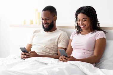 Bin yıllık Afro-Amerikan erkek ve bayanın yatak odasının içinde oturup, telefonda sohbet edip, internette sörf yapmalarına sevindim. Yeni uygulama, çevrimiçi oyun, cihaz bağımlılığı ve sosyal ağlar. İyi teklif, reklam.