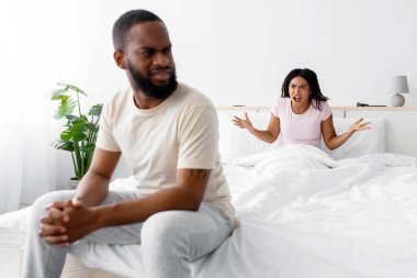 Sad young black man listen wife, woman freaking out and yells at unhappy husband, swear in bedroom interior. Covid-19 outbreak, stress, sexual dysfunction, quarrel, scandal at home, family problems