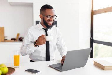 Beyaz gömlekli ve kravatlı mutlu bir milenyum adamı ofiste bilgisayarla çalışırken, laptopla masada otururken, gözlüklü yakışıklı bir adam ekranına bakarken, gülümserken, sıcak kahve içerken...