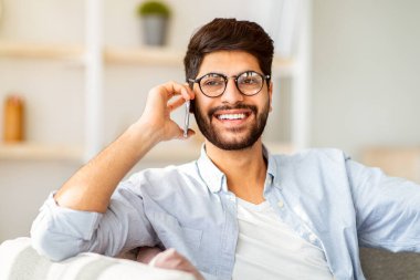 Telefon görüşmesi konsepti. Neşeli Arap adam akıllı telefonda arkadaşıyla ya da sevgilisiyle konuşuyor. İç kısımdaki kanepede dinleniyor. Gülümseyen adam keyifli bir konuşma yapıyor. Mobil iletişim konsepti
