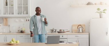 Yaralanmadan sonra evde iyileşme, uzaktan çalışma, yeni normal. Neşeli, olgun, Afro-Amerikan engelli adam tekerlekli sandalyede duruyor. Mutfakta laptopla kahve içiyor, fotokopi çekiyor.