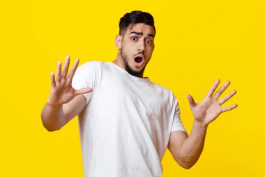 Ürkmüş ortaçağ ortadoğulu adam duruş hareketi gösteriyor, kameraya bakıyor ve el kaldırıyor, sarı stüdyo arka planı, kopyalama alanı. İnsani jestler ve duygular kavramı