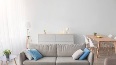 Dairesinde kimse yok, minimalist tarzda ve içerisi hakkında güncel blog yazmıyor. Renkli yastıklı gri kanepe, koltuk, halı, masa, arka planda perde olan pencere, İskandinav oturma odası