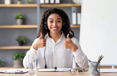 Mükemmel çalışma sonucu, olumlu duygular ve uzak eğitim. Binlerce yıllık mutlu Afro-Amerikan kadın kara tahta arka planda kulaklıklarla webcam 'e bakıyor ve başparmaklarını kaldırıyor.