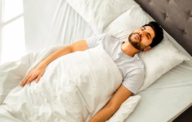 Uykusuzluk çeken mutsuz Arap adam, yatakta uzanıyor, yukarı bakıyor ve uzayı kopyalıyor. Uykusuzluk, akıl sağlığı sorunu, erkek depresyonu konsepti. Yüksek açılı görünüm