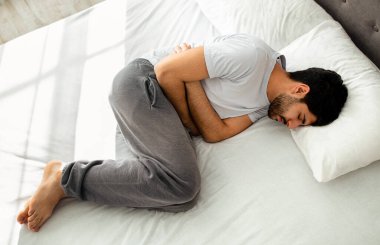 Karnım ağrıyor. Genç Arap adam karın ağrısı çekiyor. Karnına dokunuyor. Evde yatarken karnına dokunuyor. Sağlık problemi, karın iltihabı ve gastrit, apandisit konsepti