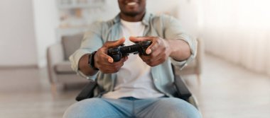 Sanal gerçeklik gözlüklerinin, üç boyutlu gözlüklerin ve evdeki oyun alanının tadını çıkarıyor. Gülümseyen Afrikalı Amerikalı sakat bir adam tekerlekli sandalyede bilgisayar oyunu oynuyor. Oturma odasında joystick ile oynuyor.