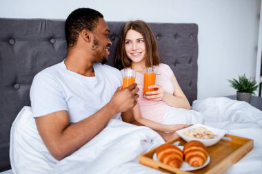 Çok ırklı çifti sevmek yatakta kahvaltı yapmak, balayı sabahını otelde geçirmek. Genç çok ırklı yeni evliler lezzetli yemeklerle romantik zamanların tadını çıkarıyorlar.