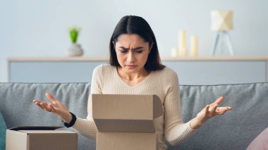 Negatif kötü duygular, yanlış alım, teslimat hatası ya da hasarlı paket. Huysuz, mutsuz bir Arap kadın, kanepeye oturur, karton kutuyu açar ve oturma odasının iç kısımlarında kollarını açar.