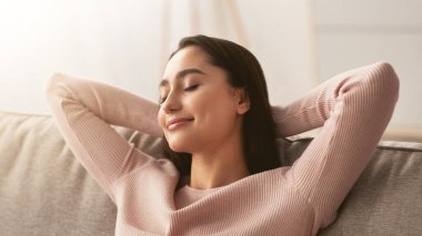 Rahat koltukta rahatla, hafta sonunun tadını çıkar. Sakin, bin yıllık, gözleri kapalı, tembel bir günde keyifli bir şeyler düşünen, hayal kuran, iç mekanda sabahları planlayan Arap bir kadın.