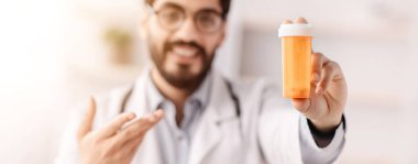 Modern ilaçlar, ilaç, ilaç, sağlık ve tedavi, doktor tavsiyesi. Beyaz önlüklü, gülümseyen, yakışıklı, sakallı adam, seçici bir odak noktası olan bir kavanoz hap gösteriyor.