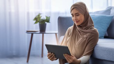 Covid-19 karantinası sırasında çalışma ofisi, evde kal ve güvende ol, virüs salgınını önlemek için izolasyon. Türbanlı genç Arap bayan, sohbet yazma sosyal ağlar içinde tablet oturma odasında iç mekanda