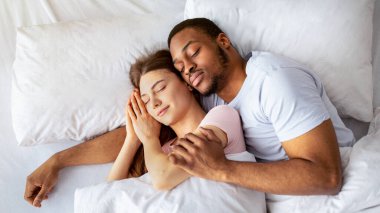 Çok kültürlü çiftler, rahat bir sabah geçiriyorlar. Uykularında birbirlerine sarılıyorlar. Genç bir ailenin yatak odasında kestirip kucaklaşırken çekilmiş bir fotoğrafı.