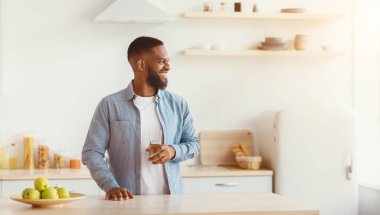 Mutfakta elinde bir bardak temiz suyla neşeli, genç, sakallı siyah adam boş alana bakıyor. Sağlık hizmetleri, diyet, harika bir reklam ve kendini tecrit süresince sunum, covid-19 tecrit