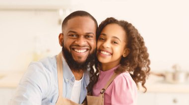 Anı yakalıyorum. Afrika kökenli Amerikalı akrabaların, önlük takıp, kameraya sarılıp, mutfakta poz verdikleri yakın bir portre. Sevecen kız sakallı babasını kucaklıyor ve gülümsüyor.