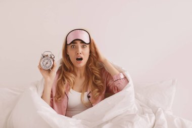 Bu kadar geç kalkmak. Uyuyakalmak, işe geç kalmak, endişe. Şok olmuş, pijama giymiş, elinde alarmlı saatle beyaz duvar arkasında uyuyakalmış sarışın bir kadın.