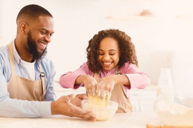 Pişirme Kavramı. Mutfakta elleri ile hamur büken neşeli zenci kızın portresi, önlük takan, kızına yardım eden neşeli baba, ev yapımı hamur işini hazırlarken ailesinin eğlenmesi.