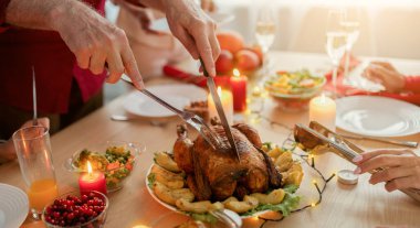 Tanınmayan son sınıf öğrencisi kavrulmuş Noel hindisini kesiyor. Çok nesildir ailesiyle birlikte Noel 'i kutluyor. Yakın plan. İçerideki büyük masada yaşlı bir erkeğin şenlikli yemekler servis edişinin görüntüsü.