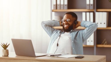 Gözlüklü ve kulaklıklı mutlu siyah sakallı adam başarılı bir anlaşmayla sevinir, rahatlar ve ofis içi dizüstü bilgisayarına bakar. Mesafeli bir iş ve karantinaya alınması gereken bir iş.