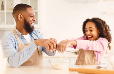 Ev Fırını Konsepti. Mutfakta birlikte yemek pişirirken gülümseyen adamla eğlenen siyah kız, tatlı kızıyla tatlı turta için sıçan neşeli baba, seçici odaklı,