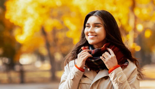 Paltolu ve sıcak atkılı güzel bir milenyum hanımefendisi sonbahar parkında rengarenk mevsimlerin tadını çıkarıyor. Gülümseyen genç kadın güneşli bir sonbahar gününde dışarıda yürüyor.