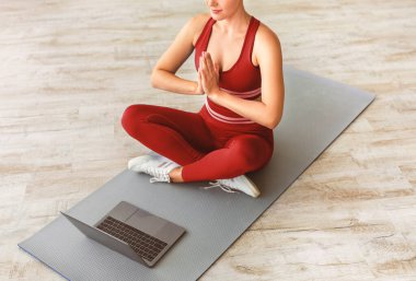 Sakin ol, meditasyon, sağlıklı yaşam tarzı. Yüksek açılı üst bakış açısıyla, gözleri kapalı bir kadın, asma nilüfer pozisyonunda yoga minderinde oturmuş, dua ederken bilgisayarın el ele tutuşunu kullanıyor.
