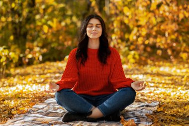 Güzel bir sonbahar parkında meditasyon yapan konsantre genç bir kadın. Sakin bir milenyum hanımı sabah yoga çalışmasını dışarıda yapıyor. İç uyumu ve huzuru sağlıyor. Zihnini ve vücudunu geliştiriyor.