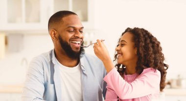 Sevimli Afrikalı Amerikalı küçük kızın portresi. Onlar evde kahvaltılarını yaparken mutlu babasını mısır gevreğiyle besliyor. Bağlanma, Sevgi, Babalık ve Aile Kavramı